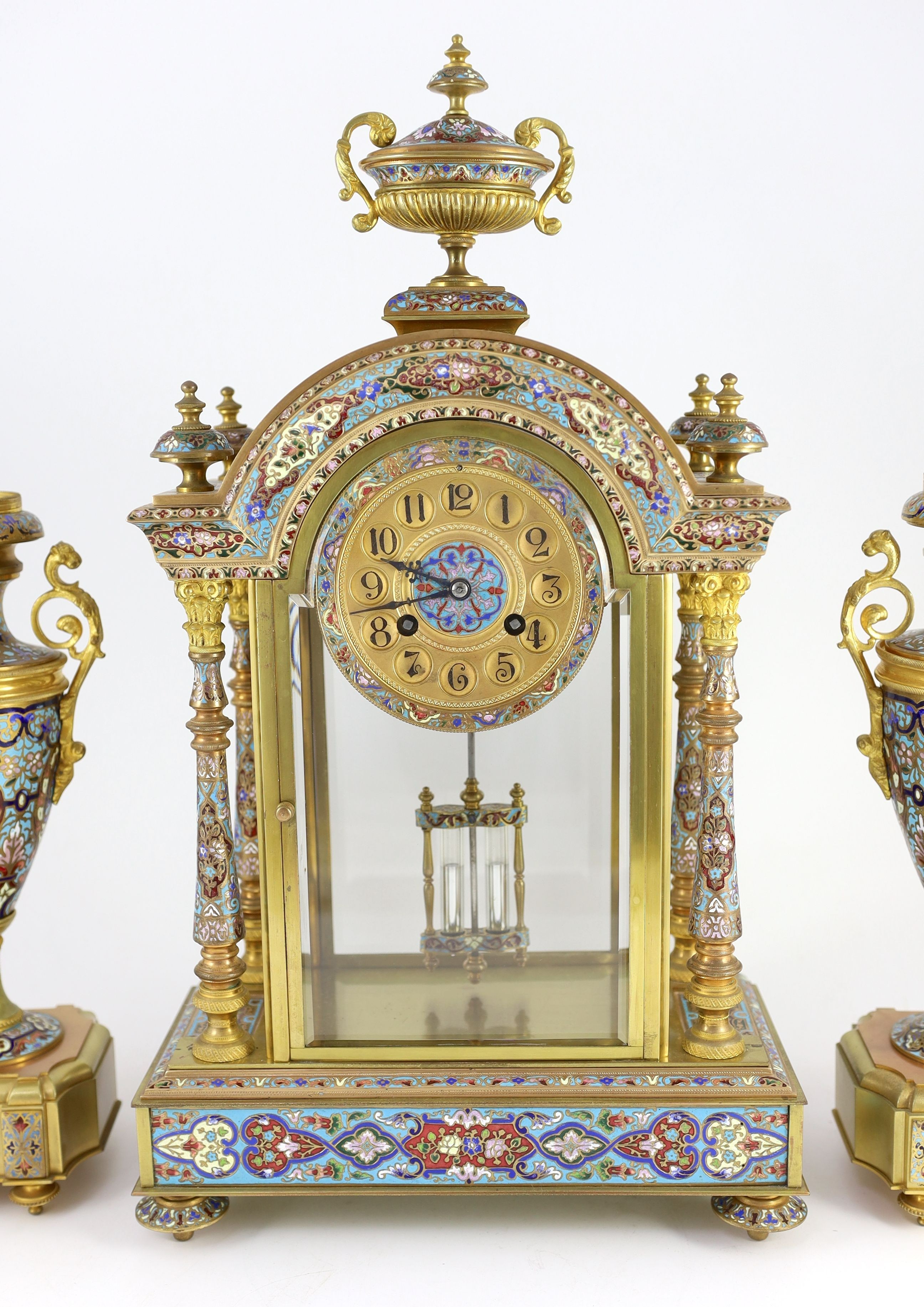 An early 20th century French ormolu and champleve enamel clock garniture, clock: height 50.5cm urns: height 32.5cm